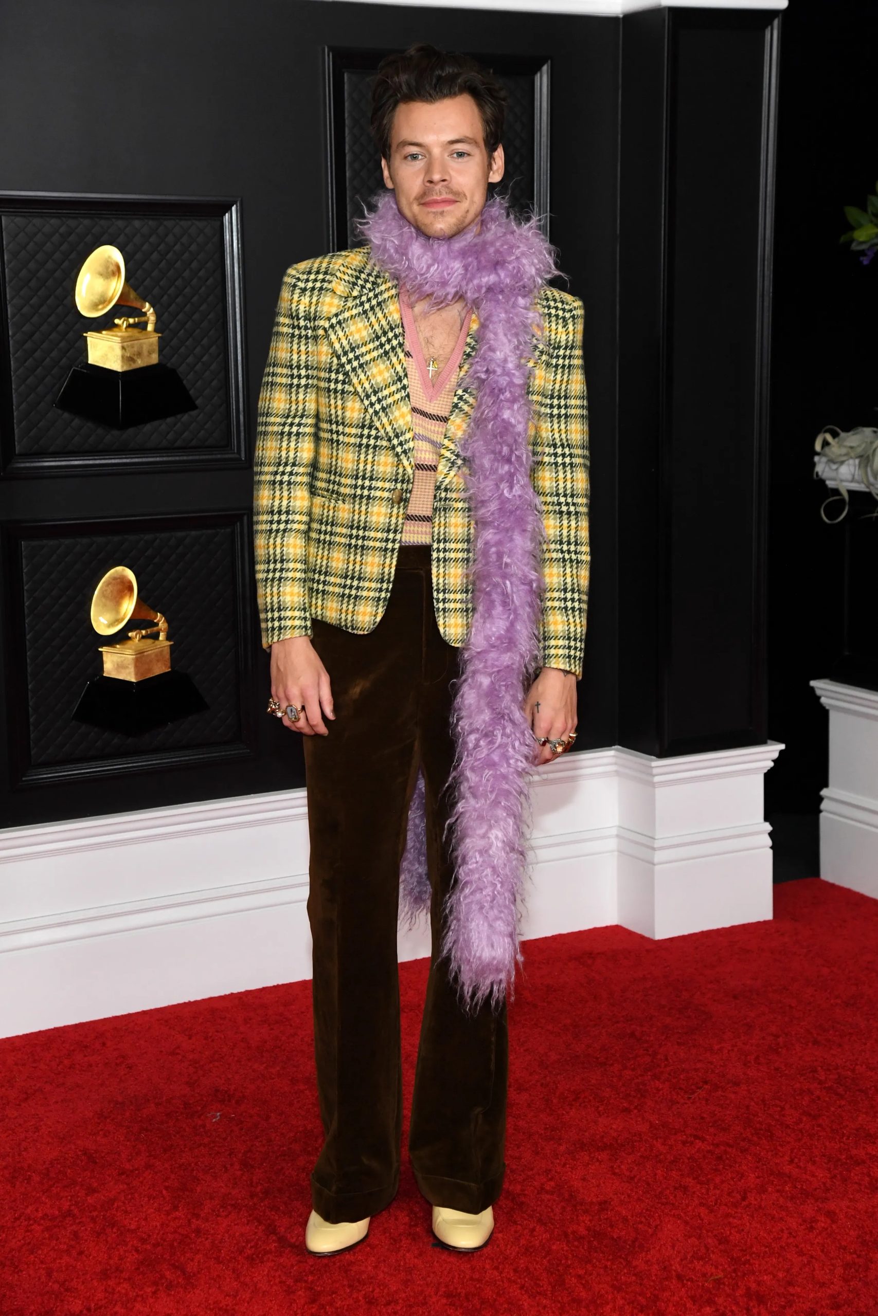 Voor de rode loper van de Grammy's was Styles gehuld in een Gucci-look bestaande uit een ruitjesjas met een bruine uitlopende broek, een gebreide tanktop en een paarse boa, maart 2021.