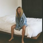 Model zit op bed en draagt een denim blouse.