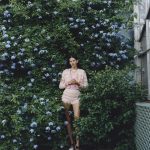 Model staat in een bloemenstruik.