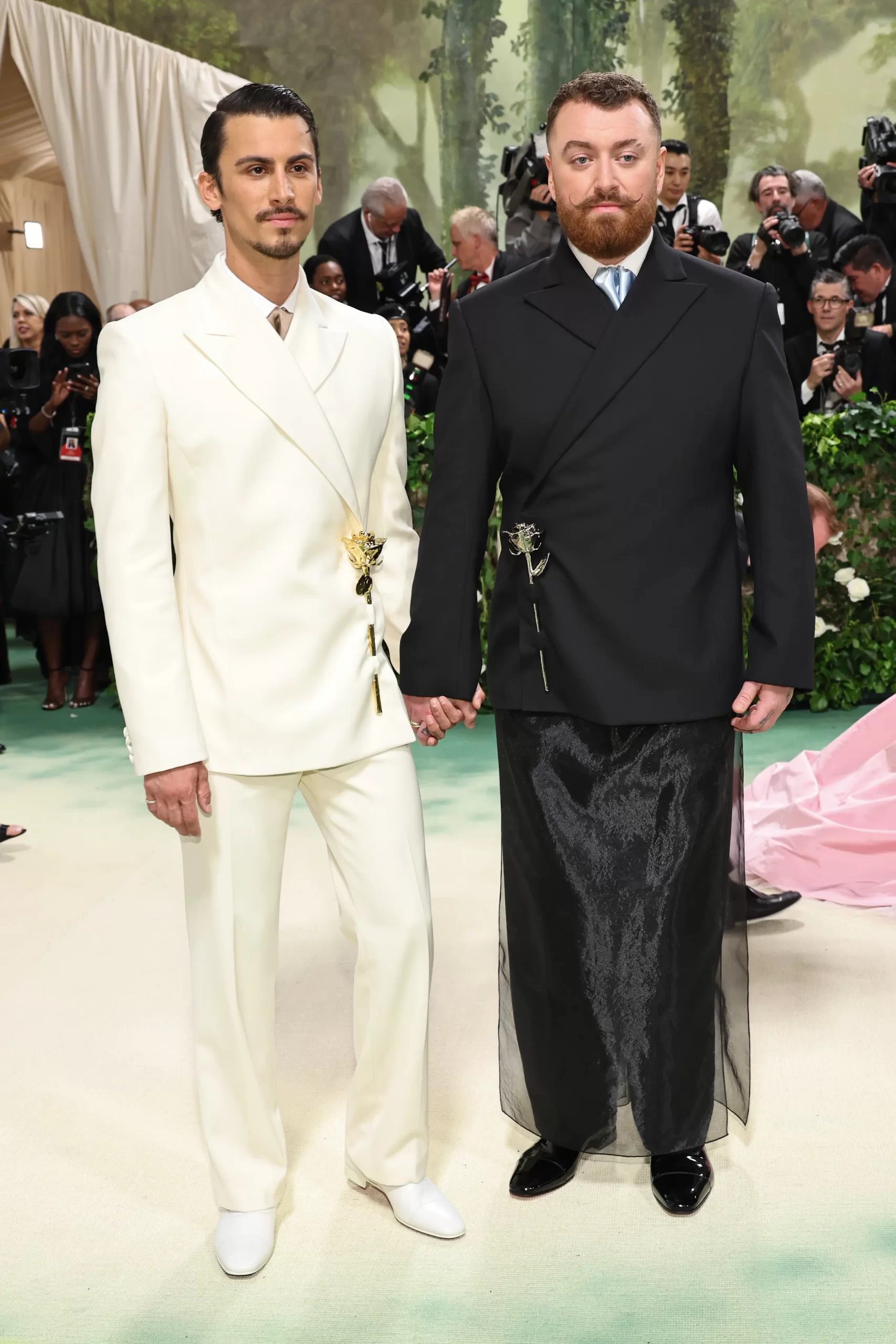 Christian Cowan in een wit pak en Sam Smith in een zwarte blazer met rok en roosdetail