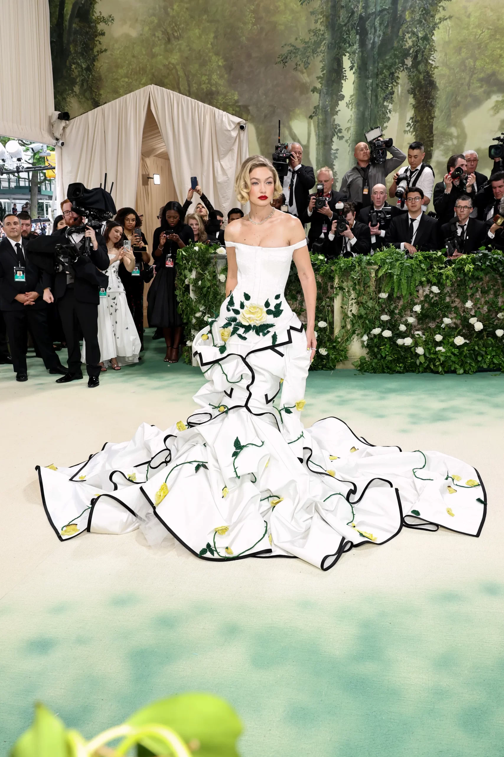 Gigi Hadid draagt een lange witte jurk met zwarte details en gele bloemen
