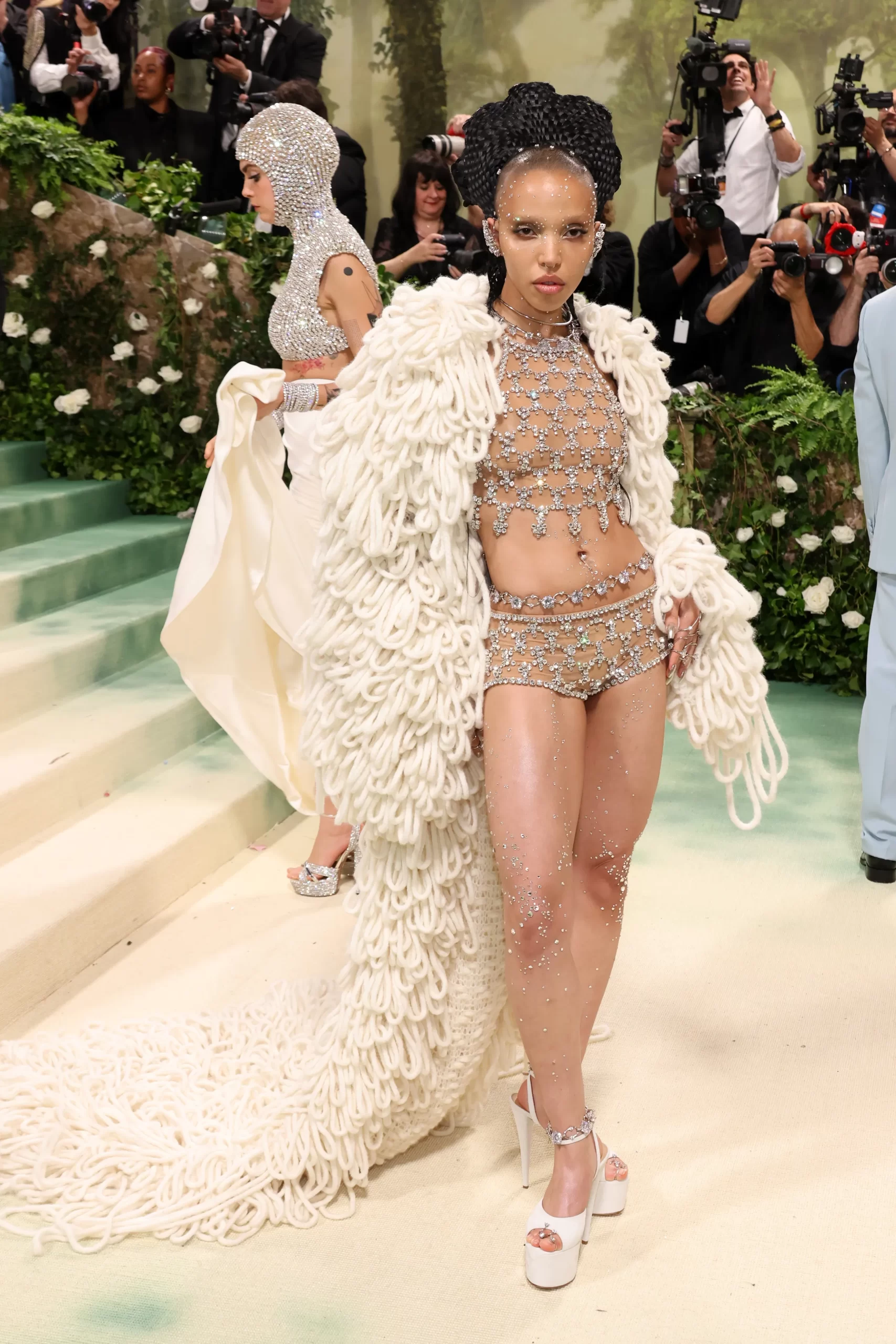 FKA Twigs in een doorschijnend ensemble met juwelen en een lange fluffy cape