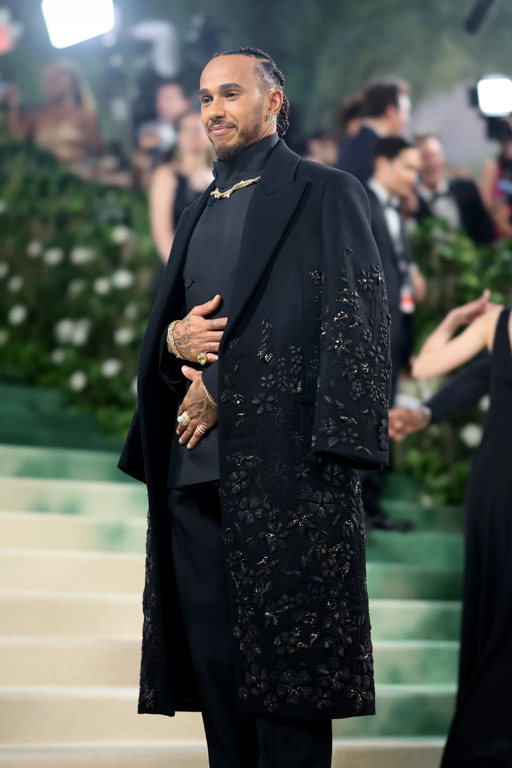 Lewis Hamilton in een zwart pak met lange jas en bloemendetails op het Met Gala 2024