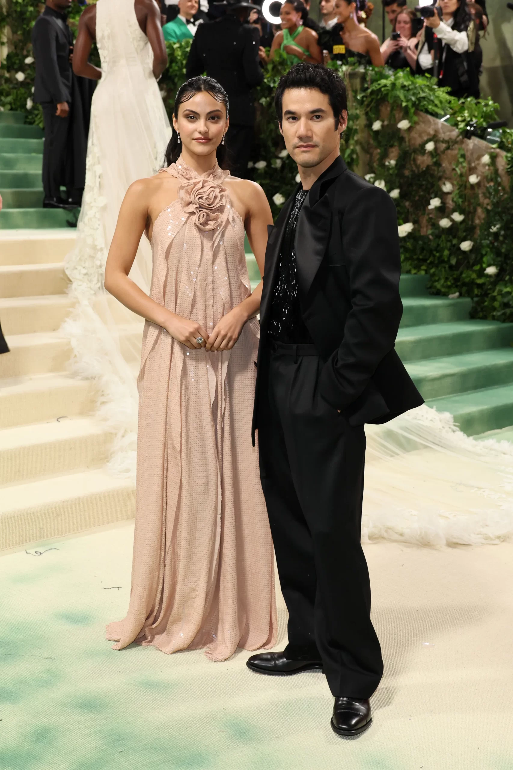 Camila Mendes in een nude jurk met bloemdetail en Joseph Altuzarra in een zwart pak