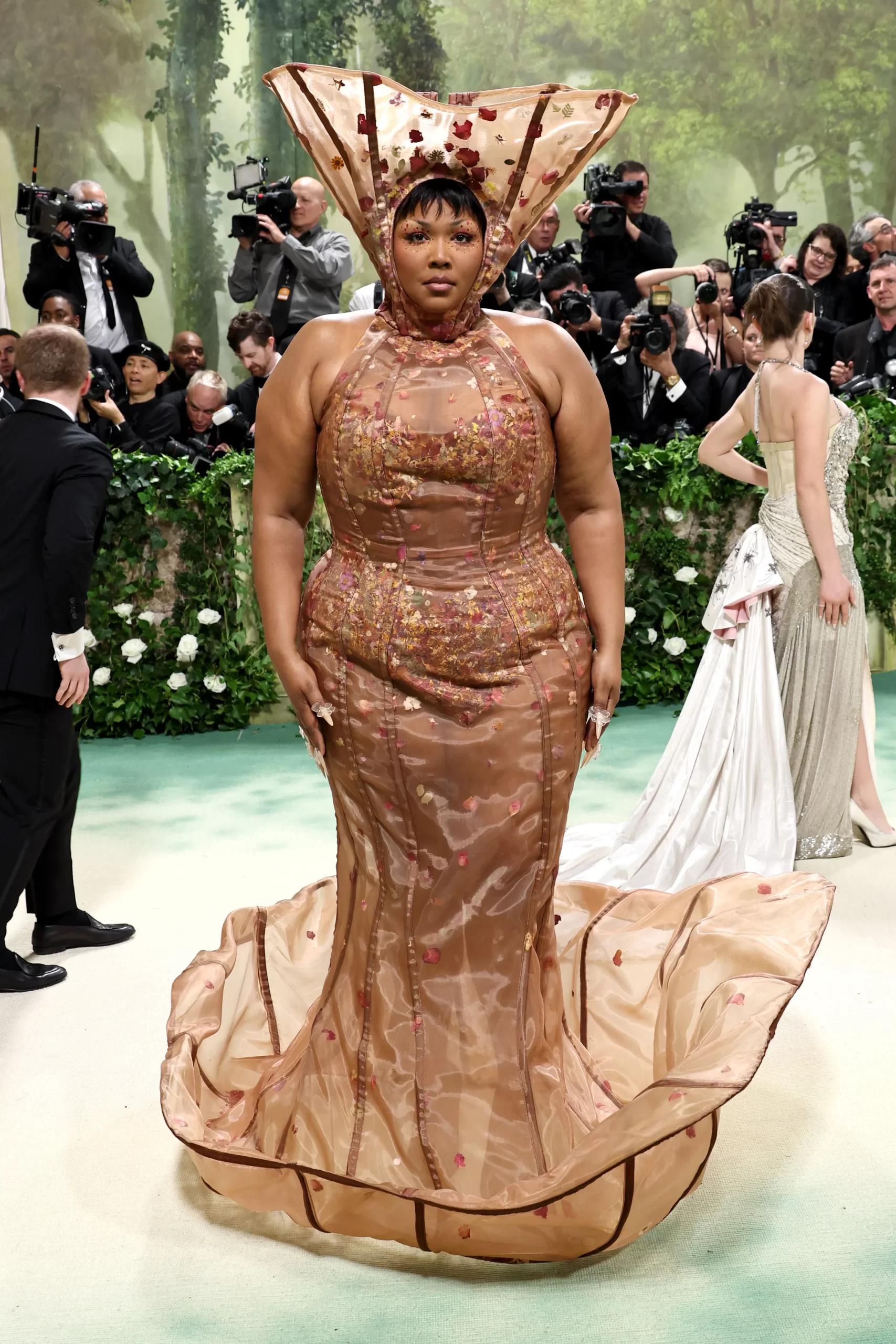 Lizzo in een nude-kleurige nauwsluitende jurk met opgeheven zoom en bloemendetails