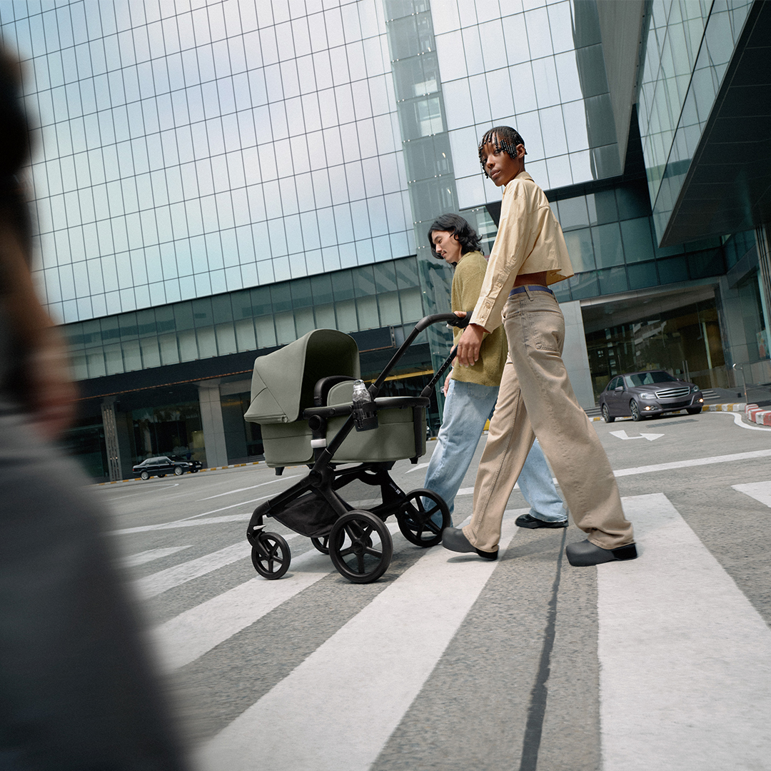 Twee mensen met een kinderwagen lopen over een zebrapad