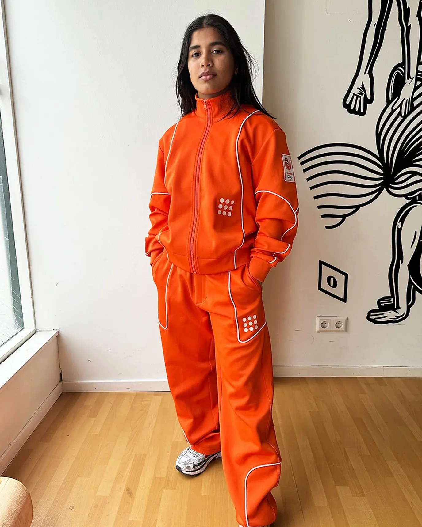 Breakdancer India Sardjoe draagt een oranje trainingspak uit de collectie van The New Originals
