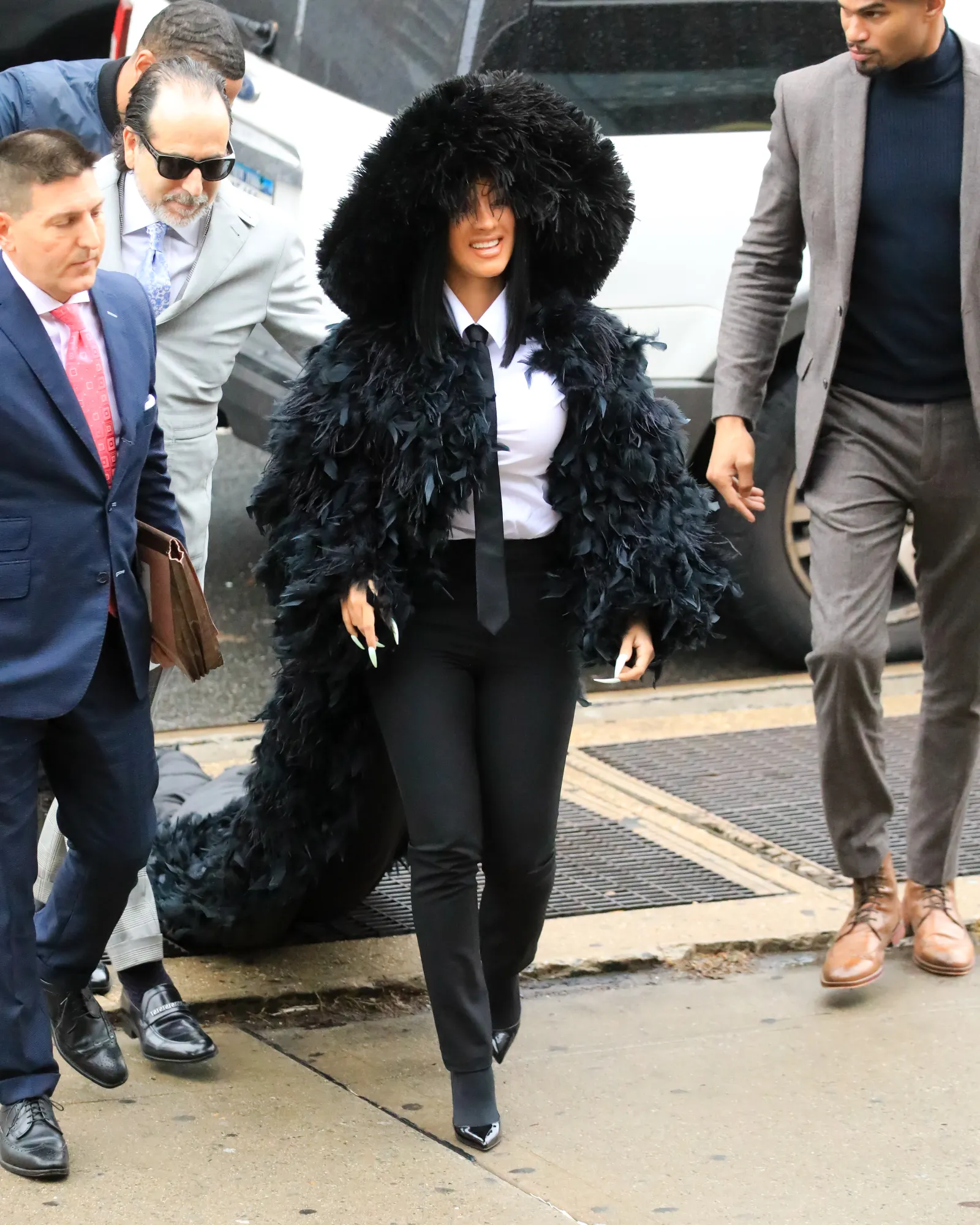 Cardi B in een donzige zwarte manteljas en hoed bij de rechtbank