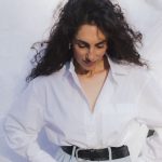 Gisele Azad in een witte blouse en een lichtblauwe broek met riem