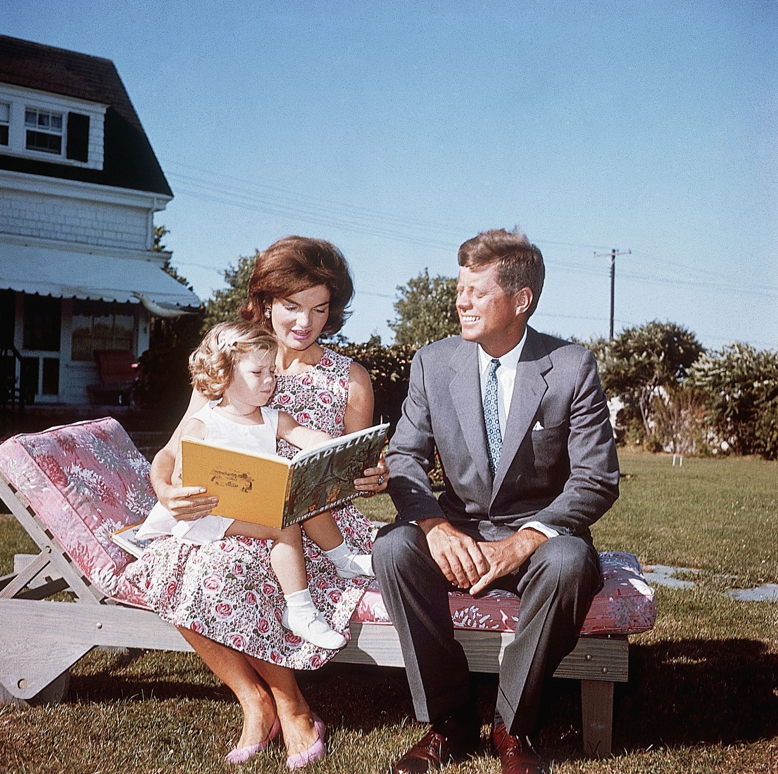 Jackie Kennedy en John F. Kennedy zitten op een ligstoel bij hun zomerhuis terwijl ze hun dochter Caroline voorlezen.