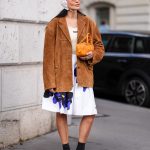 PARIS, FRANCE - OCTOBER 01: A guest wears dark brown sunglasses, white textured cap, dark brown suede oversized Miu Miu blazer jacket, cream tank top, white loose purple floral pattern/print Miu Miu over the knee skirt, shiny dark orange Miu Miu leather bag, black socks shiny dark brown loafer moccasin leather shoes, outside Miu Miu, during the Paris Fashion Week Spring/Summer 2025 on October 1, 2024 in Paris, France (Photo by Edward Berthelot/Getty Images)